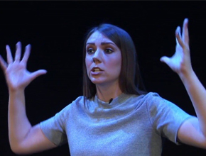 Performer silhouetted with spotlight on her, hands in the air, acting